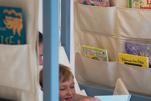 a person reading to a small child in a tent with pockets for books. Photo.