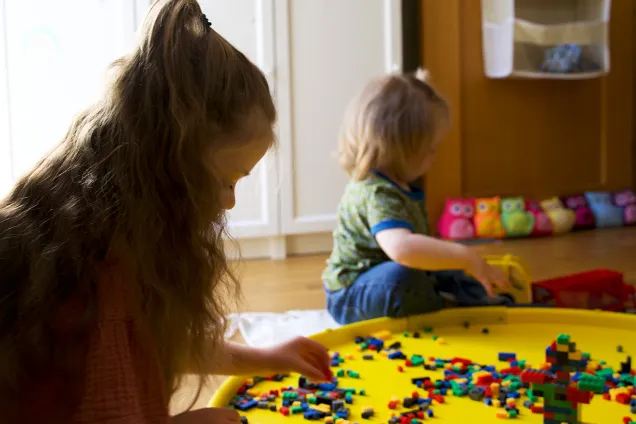 children playing with lego on a large yellow surface. 