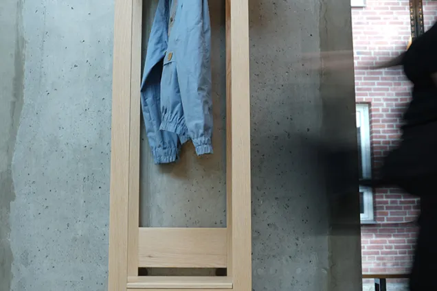 A tall and slim construction in ash wood with two shelves and a rod. Photo. 