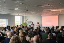 People seated in a large room facing two people standing up giving a presentation. Photo.