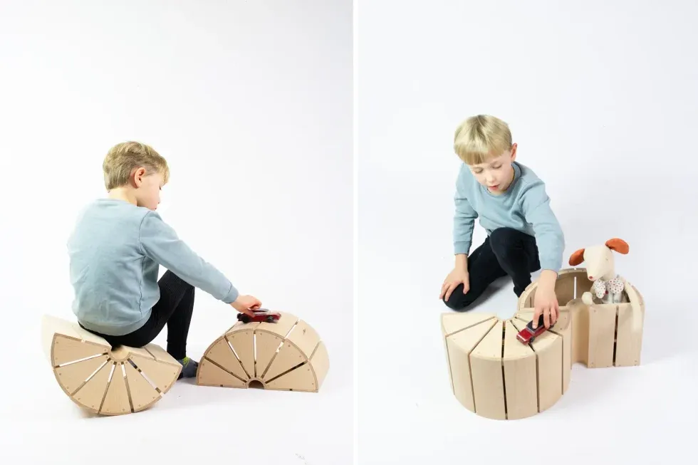 child playing with two wooden modules in different ways, as storage, seating or surface